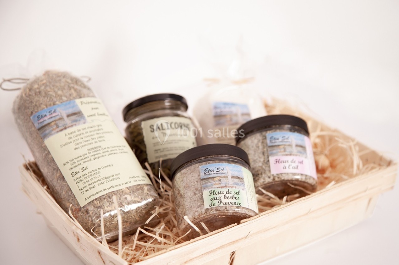 Panier en bois contenant des pots et sachets de sels aromatisés et d'épices, présentés sur un lit de paille.
