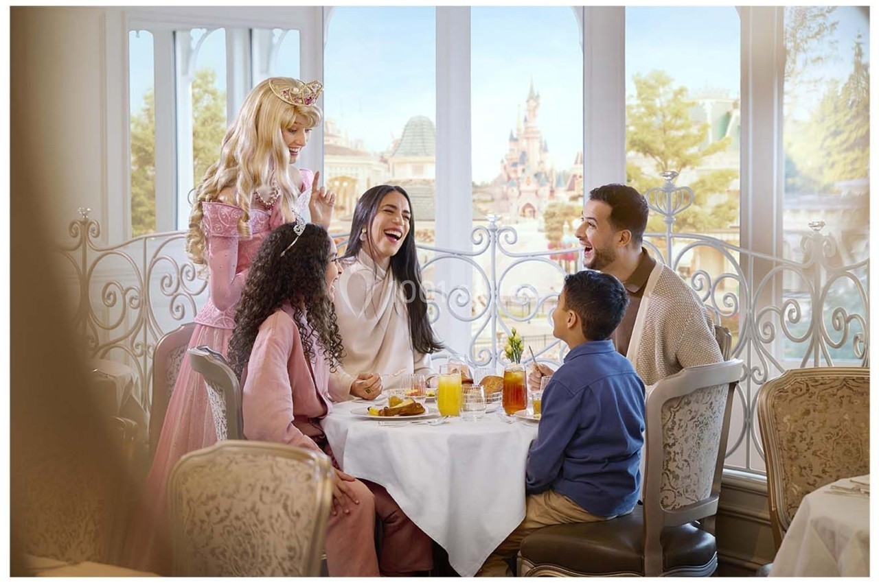 Une famille partage un repas dans un restaurant lumineux, accueillie par une femme déguisée en princesse.