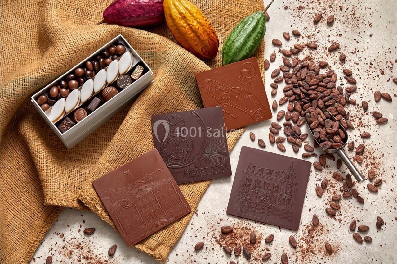 Tablettes de chocolat gravées, boîte de chocolats, fèves de cacao et poudre sur toile de jute.