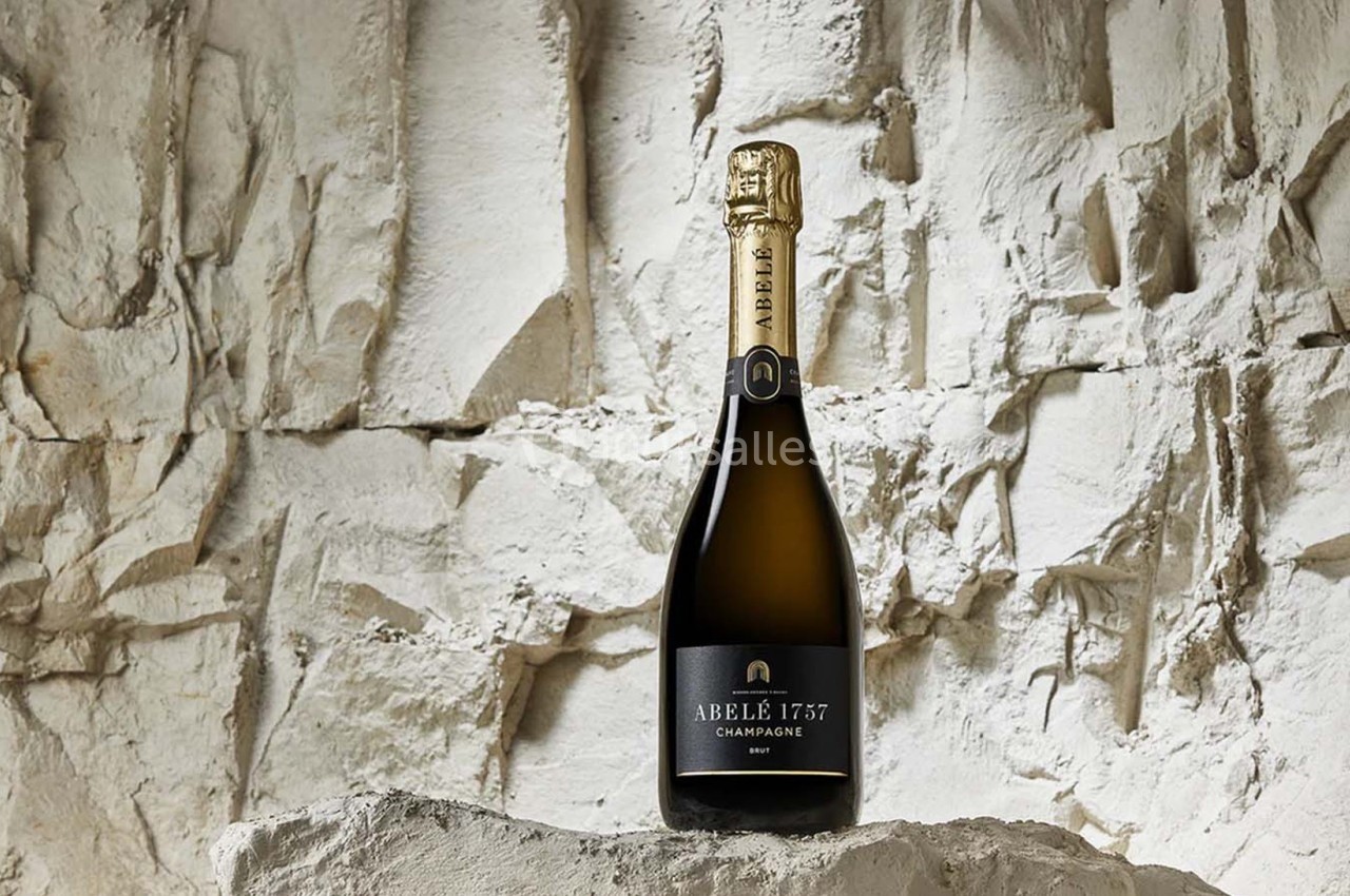Bouteille de champagne Abelé 1757 posée sur un rocher devant un mur de pierre blanche.