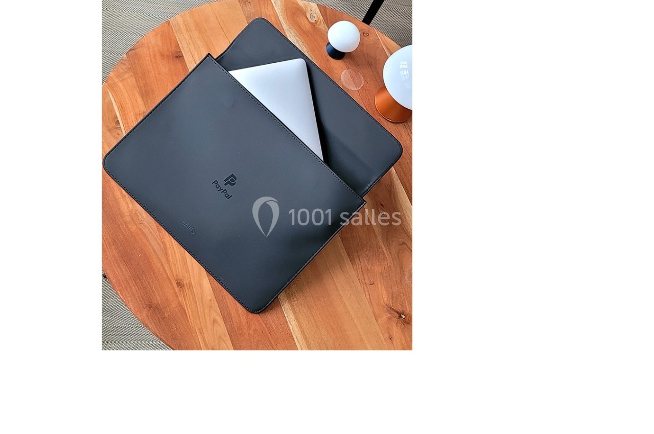Ordinateur portable argenté partiellement glissé dans une housse noire posée sur une table en bois.