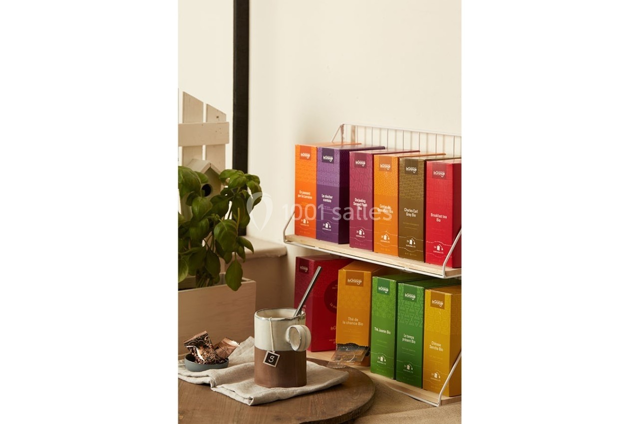 Boîtes de thé colorées alignées sur une étagère, avec une tasse de thé et une plante en arrière-plan.