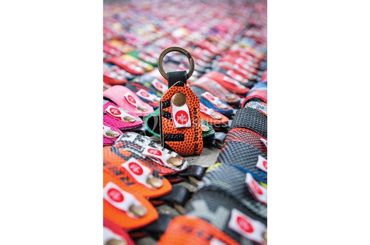 Porte-clés en cuir orange avec un anneau métallique, posé parmi d'autres porte-clés colorés disposés en arrière-plan.