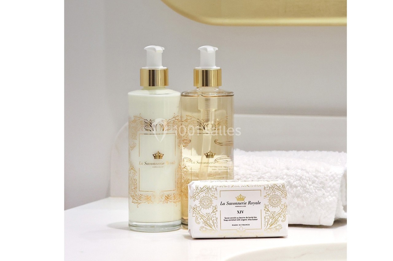 Deux flacons de savon liquide et un savon solide décorés, posés près d'une serviette blanche dans une salle de bain.