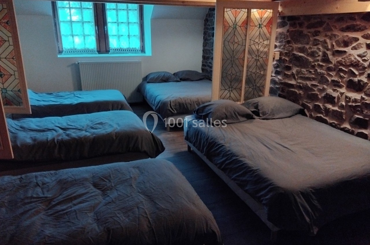 Chambre avec quatre lits doubles, murs en pierre, fenêtres à vitraux et éclairage naturel tamisé.
