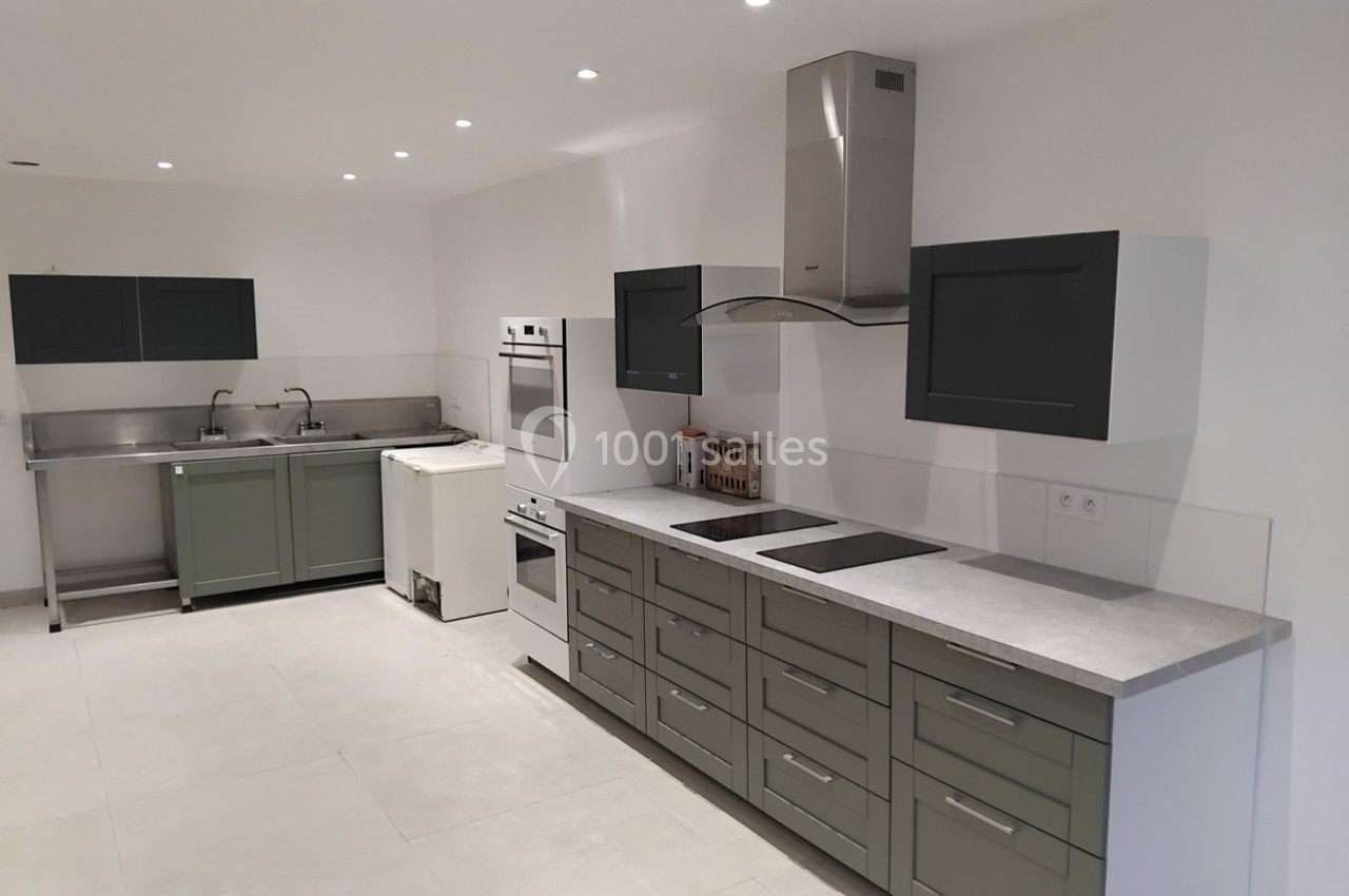 Cuisine moderne avec meubles verts, plan de travail clair, plaques de cuisson, hotte et évier en inox.