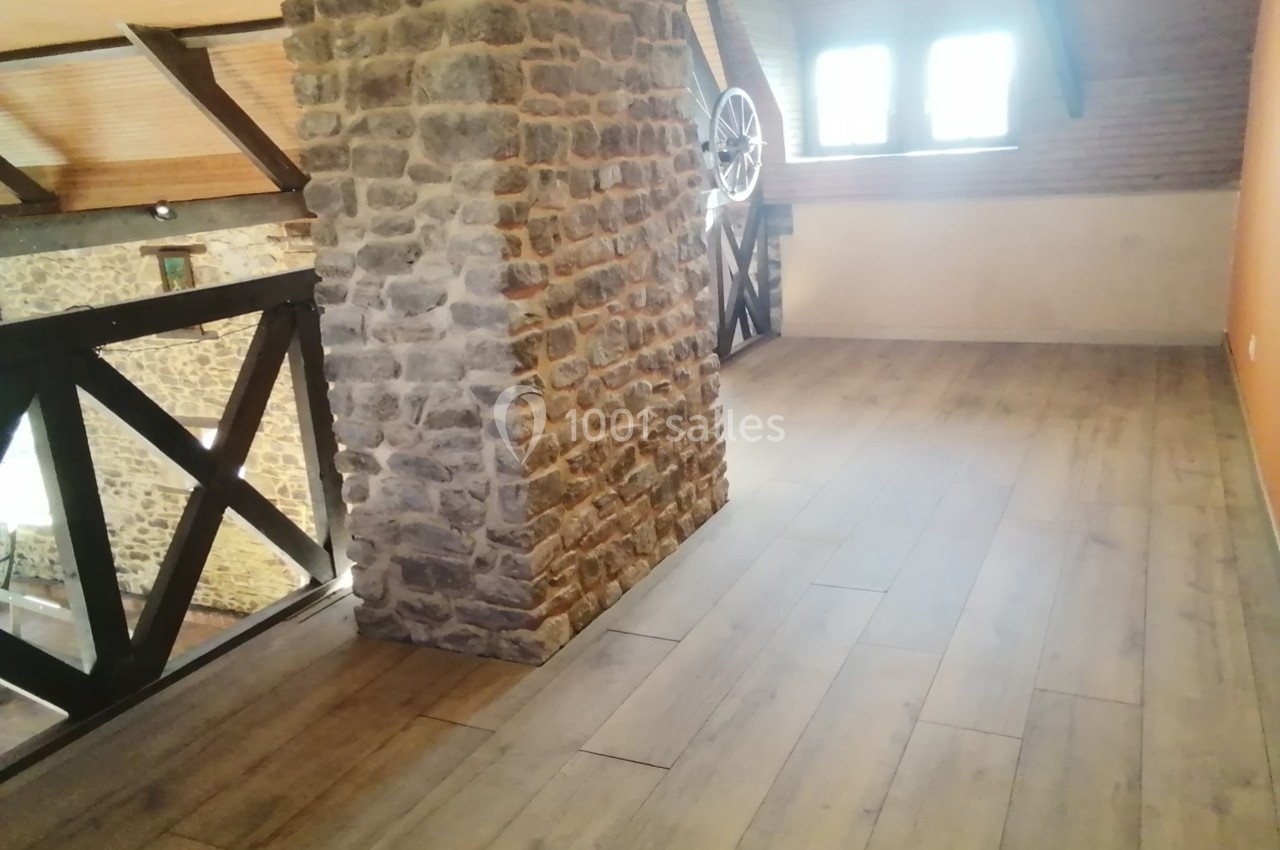 Plancher en bois clair dans une mezzanine avec murs en pierre et poutres apparentes, éclairée par une fenêtre.