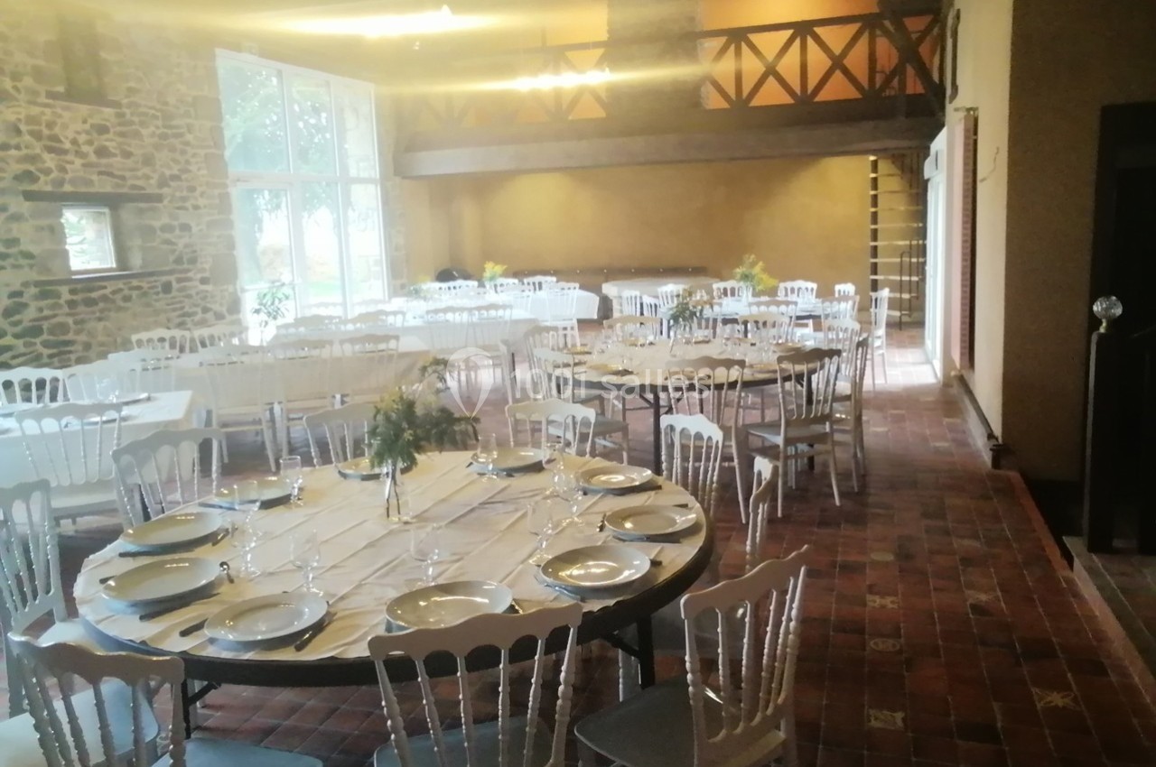 Salle de réception lumineuse avec tables rondes et chaises blanches, décorée pour un événement.