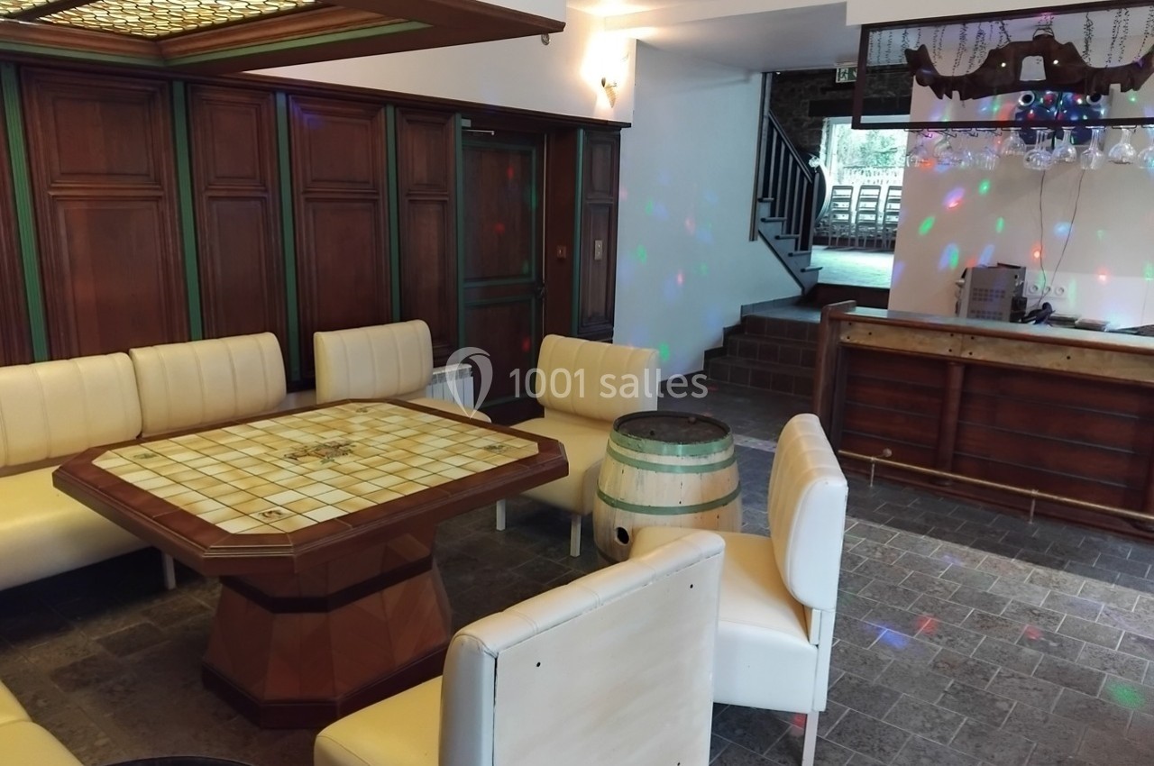 Salle avec des fauteuils blancs, une table centrale en bois avec plateau de jeu et un bar en arrière-plan.