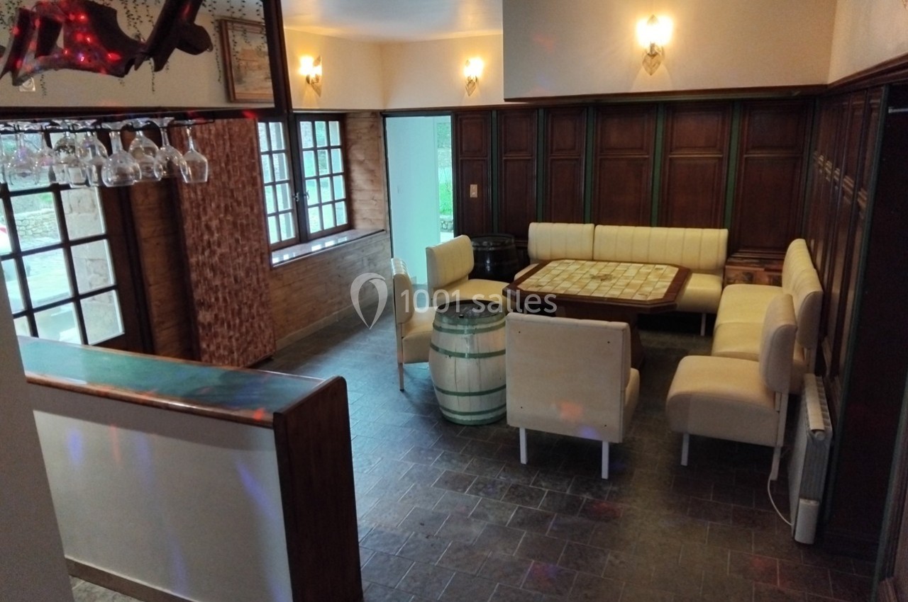 Salle avec banquettes crème autour d'une table en bois, décorée de murs en bois sombre et éclairée par des appliques murales.