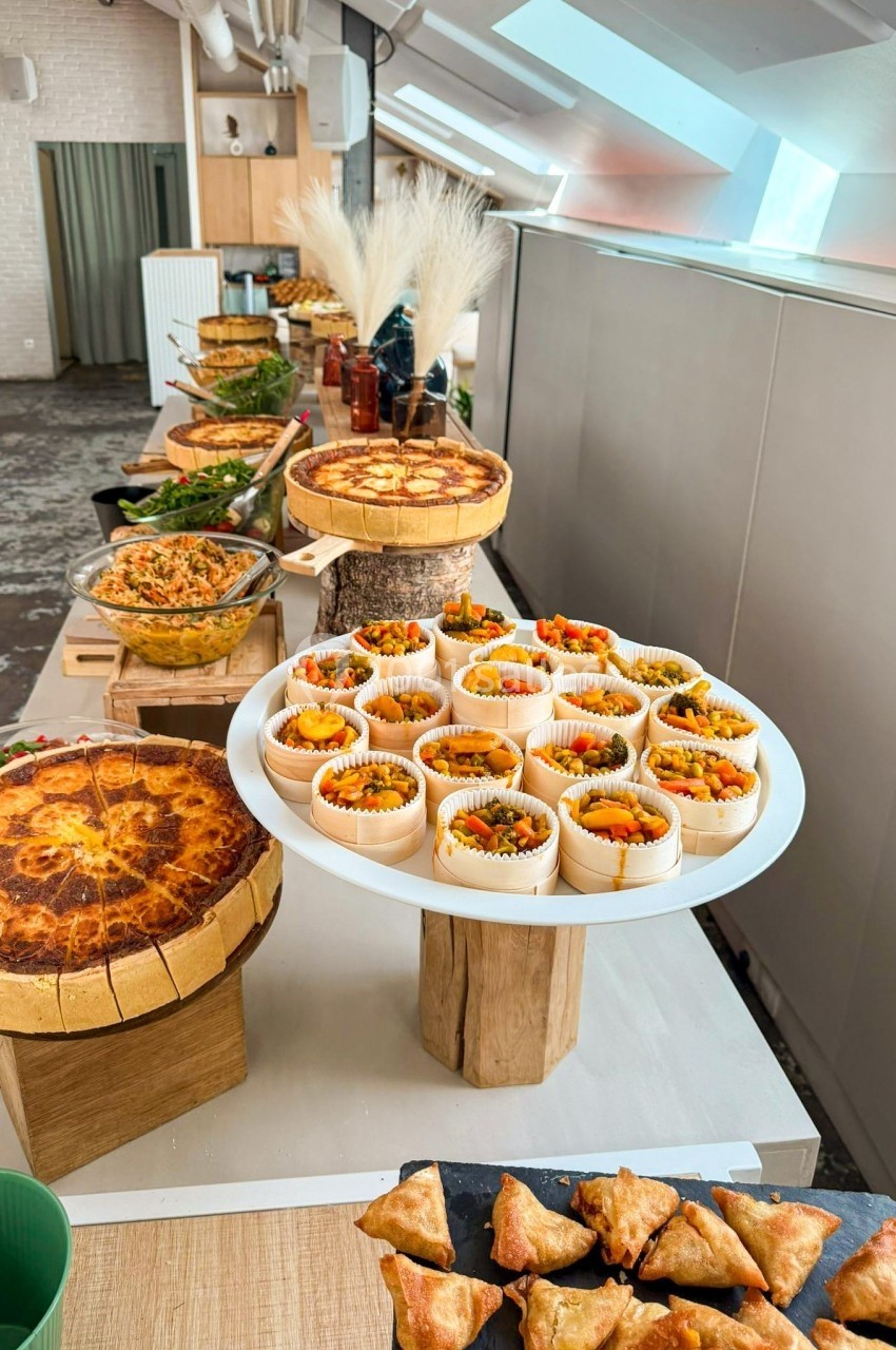 Buffet composé de quiches, samoussas, salades et verrines colorées, présenté sur une table dans un espace lumineux.
