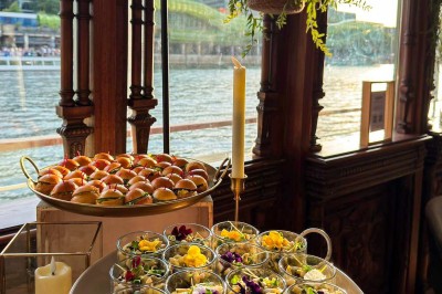 Miniature Traiteur Paris 20 (Paris) - Atelier des Sens #39 Table garnie de plats variés, incluant charcuterie et fromages, installée en extérieur près d'un plan d'eau.