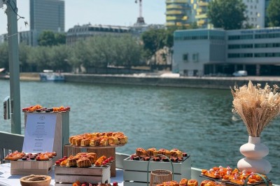 Miniature Traiteur Paris 20 (Paris) - Atelier des Sens #40 Table garnie de plats variés, incluant charcuterie et fromages, installée en extérieur près d'un plan d'eau.