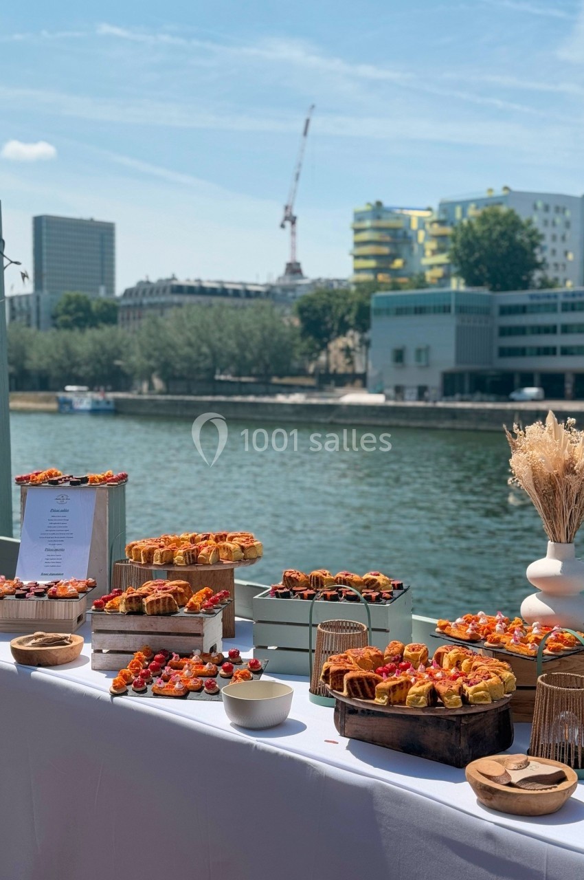 Buffet en extérieur avec vue sur une rivière, composé de plats variés disposés sur une table blanche.