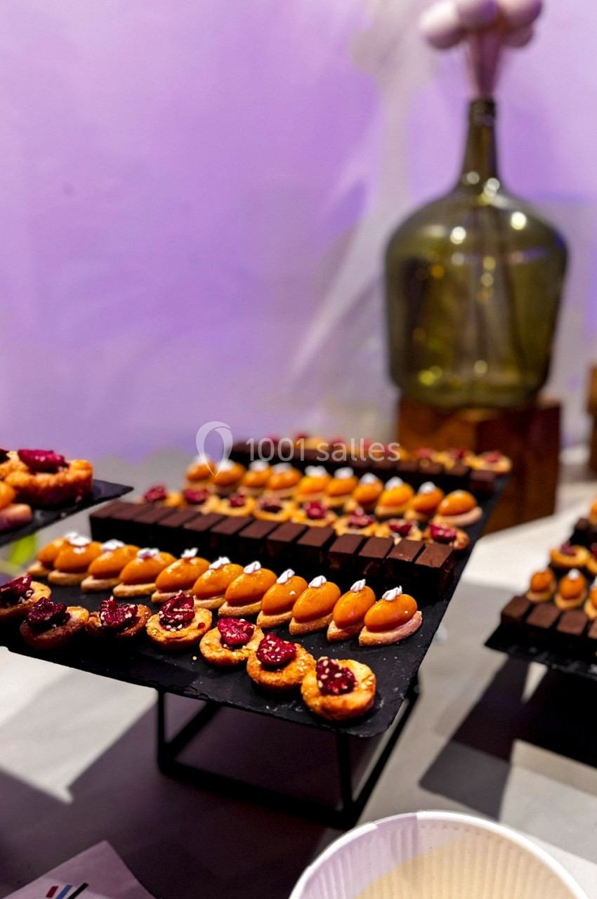 Plateaux de mignardises variées, incluant des chocolats et des pâtisseries fruitées, présentés sur des supports noirs.