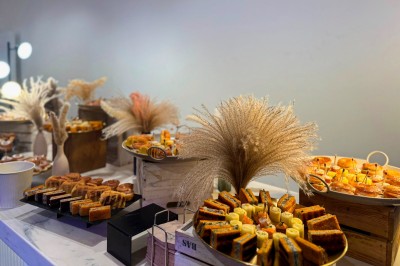 Miniature Traiteur Paris 20 (Paris) - Atelier des Sens #7 Table garnie de plats variés, incluant charcuterie et fromages, installée en extérieur près d'un plan d'eau.