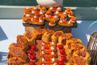 Miniature Traiteur Paris 20 (Paris) - Atelier des Sens #54 Table garnie de plats variés, incluant charcuterie et fromages, installée en extérieur près d'un plan d'eau.
