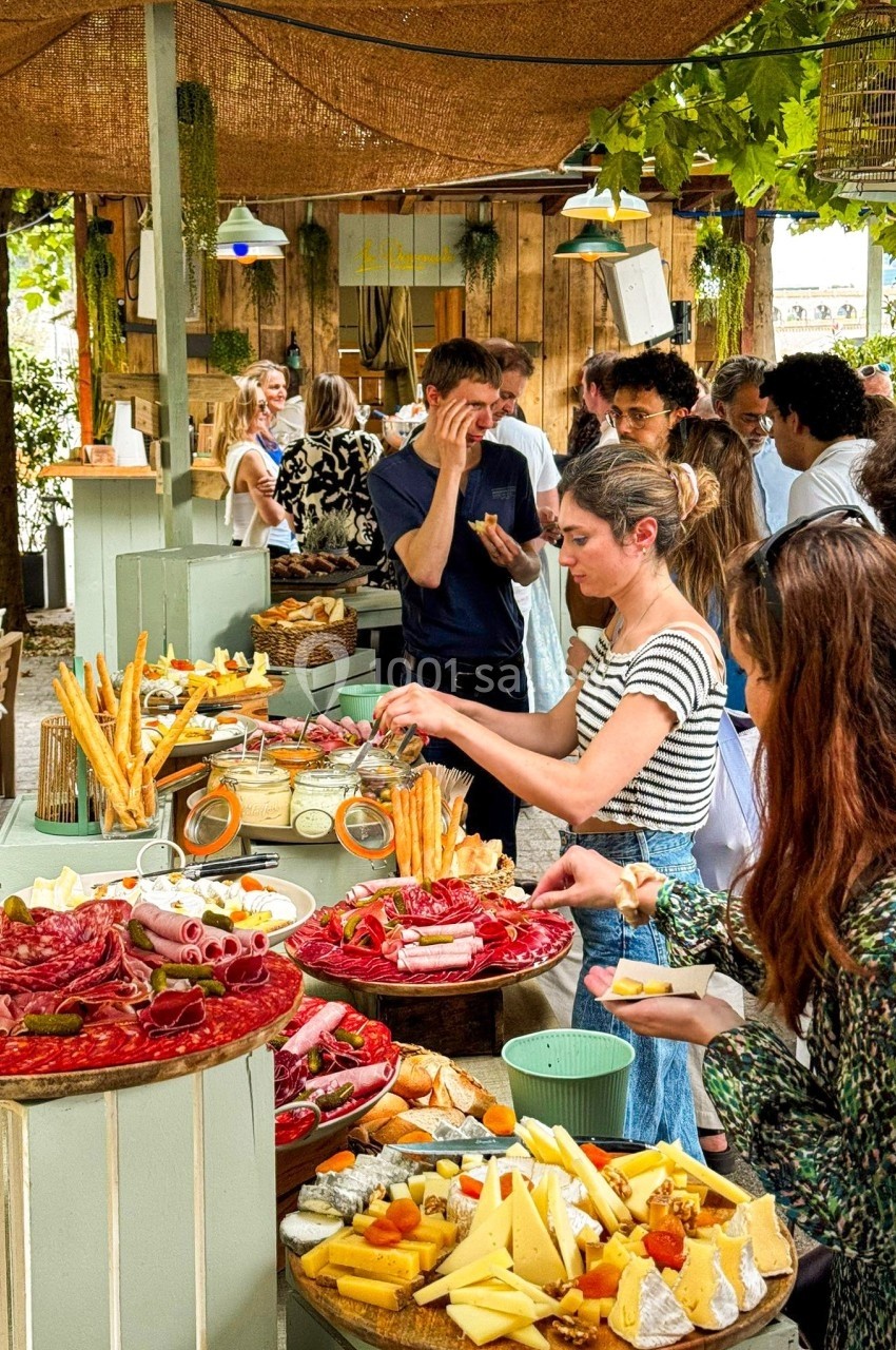 Buffet en plein air avec des plateaux de charcuterie, fromages et invités se servant dans une ambiance conviviale.