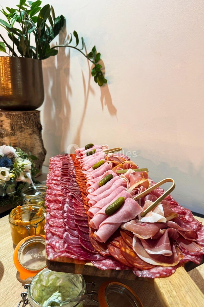 Plateau de charcuterie variée avec cornichons, présenté sur une table en bois, accompagné de pots de condiments.