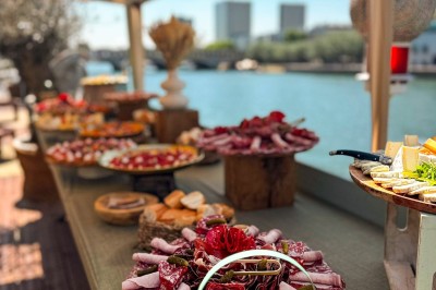 Miniature Traiteur Paris 20 (Paris) - Atelier des Sens #62 Table garnie de plats variés, incluant charcuterie et fromages, installée en extérieur près d'un plan d'eau.