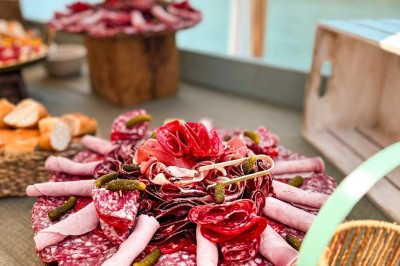 Miniature Traiteur Paris 20 (Paris) - Atelier des Sens #10 Table garnie de plats variés, incluant charcuterie et fromages, installée en extérieur près d'un plan d'eau.