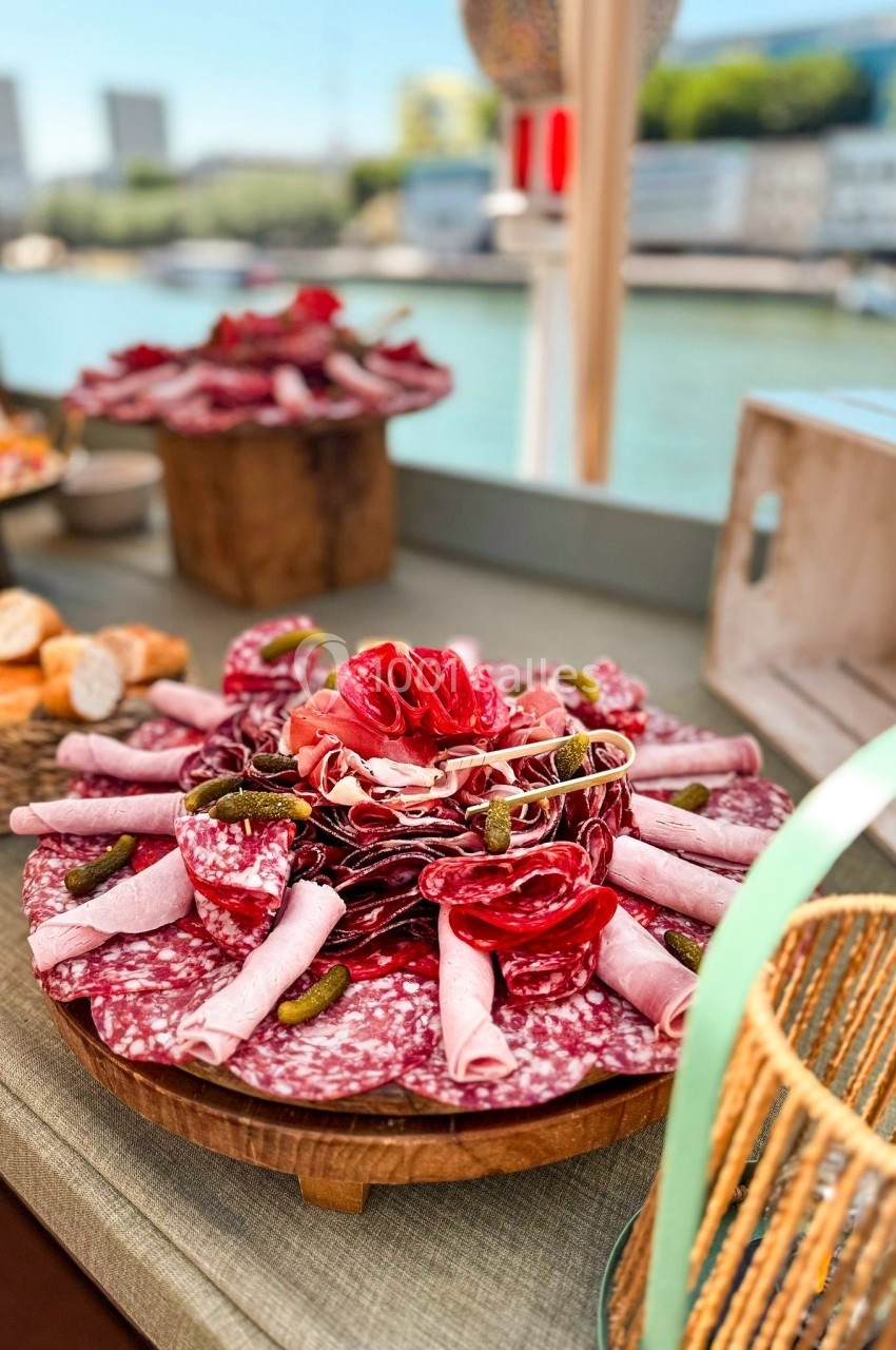 Plateau de charcuterie variée avec saucissons, jambon roulé et cornichons, présenté sur une table près d'une rivière.