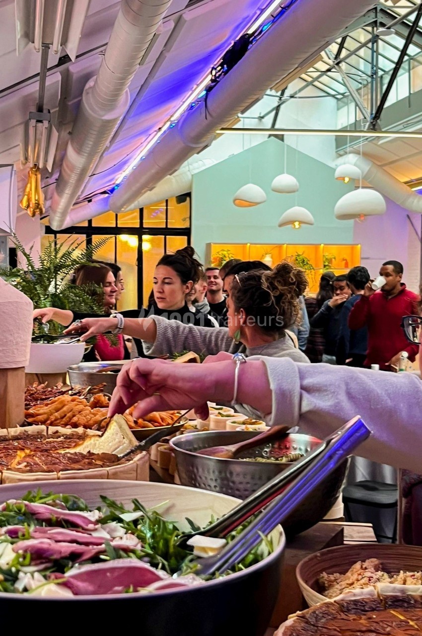 Buffet varié avec salades, quiches et plats chauds, des convives se servant dans un espace lumineux et moderne.