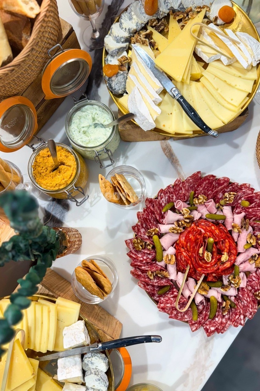 Plateau de charcuterie et fromages variés avec condiments, pain et crackers sur une table de buffet.