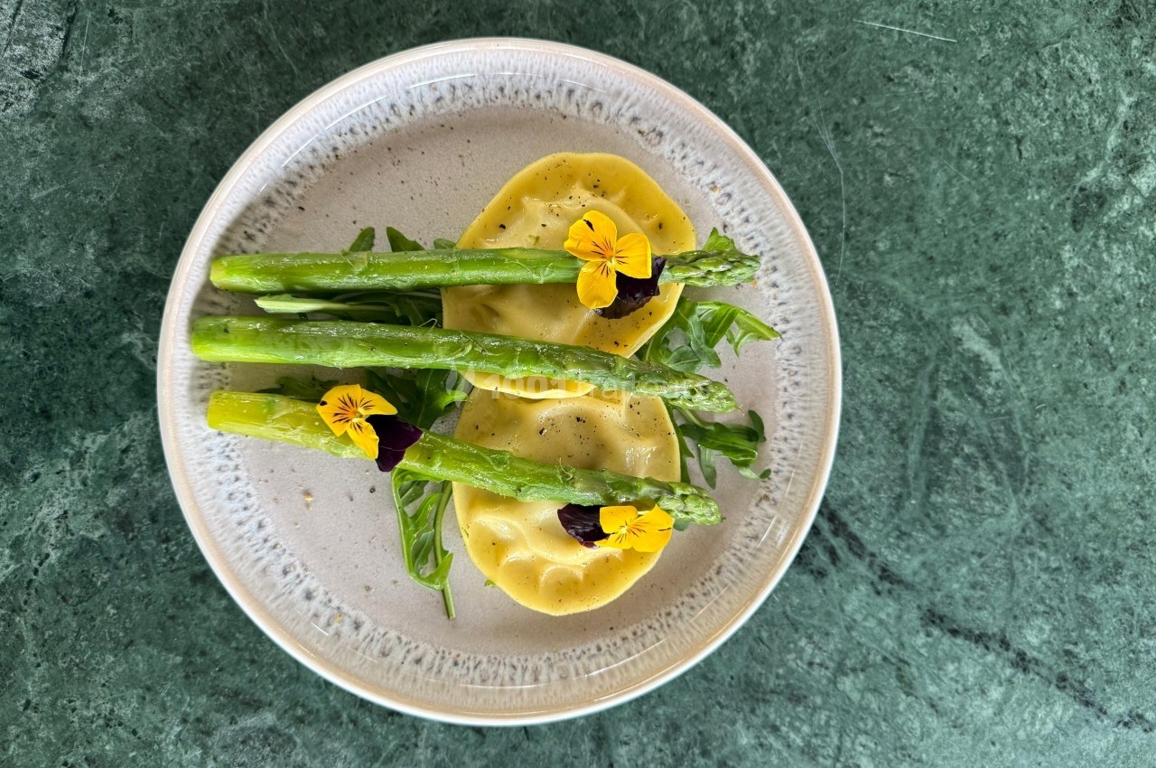 Assiette de raviolis garnis de roquette, asperges et fleurs comestibles, présentée sur une table en marbre vert.