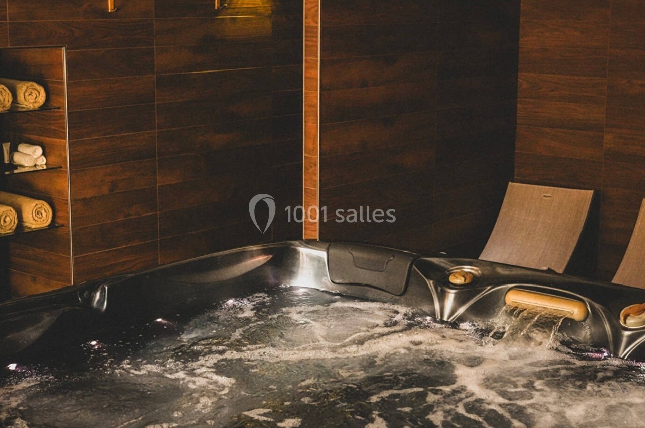 Bain à remous avec eau bouillonnante, chaises longues en bois et étagère contenant des serviettes pliées.