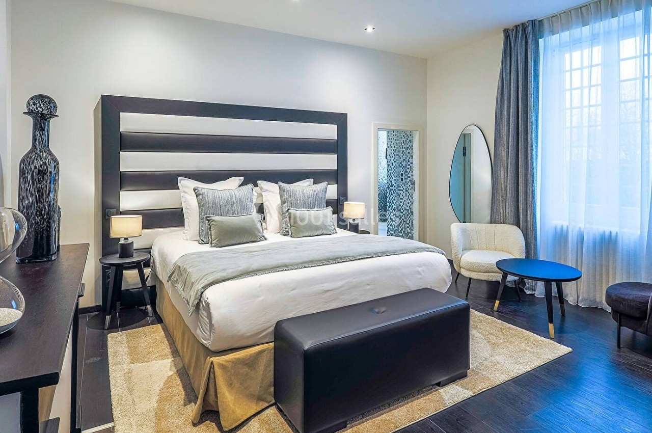 Chambre moderne avec grand lit, mobilier élégant, éclairage doux et grande fenêtre avec rideaux.