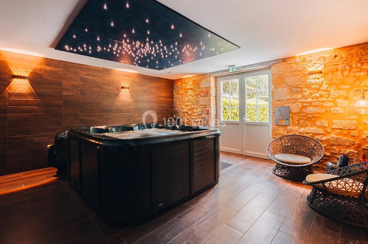 Salle avec un jacuzzi en bois, murs en pierre, fauteuils en rotin et éclairage tamisé.
