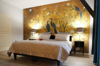 Lit à baldaquin blanc avec drapé, fauteuil rose et mur décoré de motifs floraux dans une chambre lumineuse.