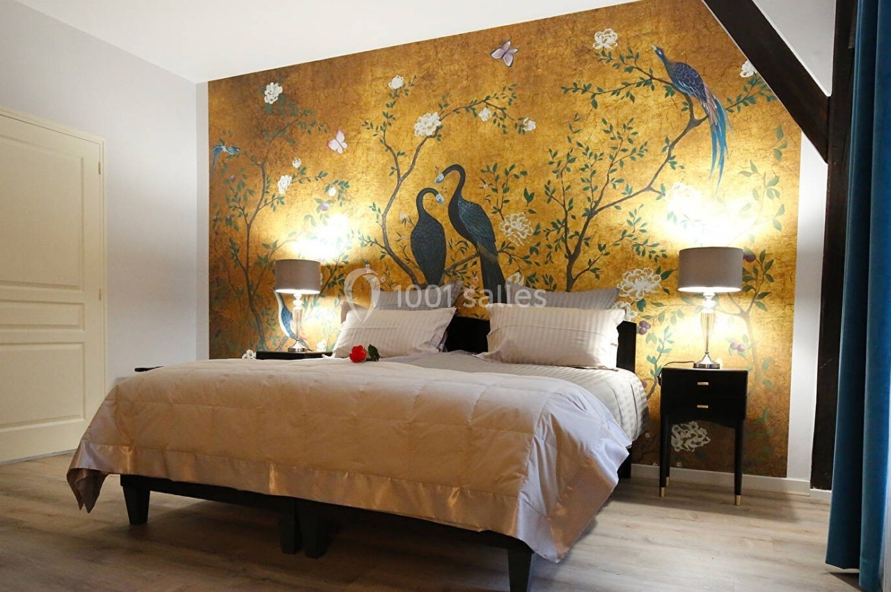 Chambre avec un lit double, mur décoré d'une fresque dorée avec des oiseaux, éclairée par deux lampes de chevet.