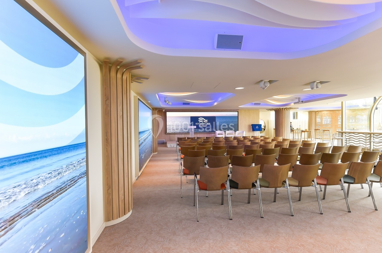 Salle de conférence lumineuse avec rangées de chaises, écran principal et décorations sur le thème de la mer.
