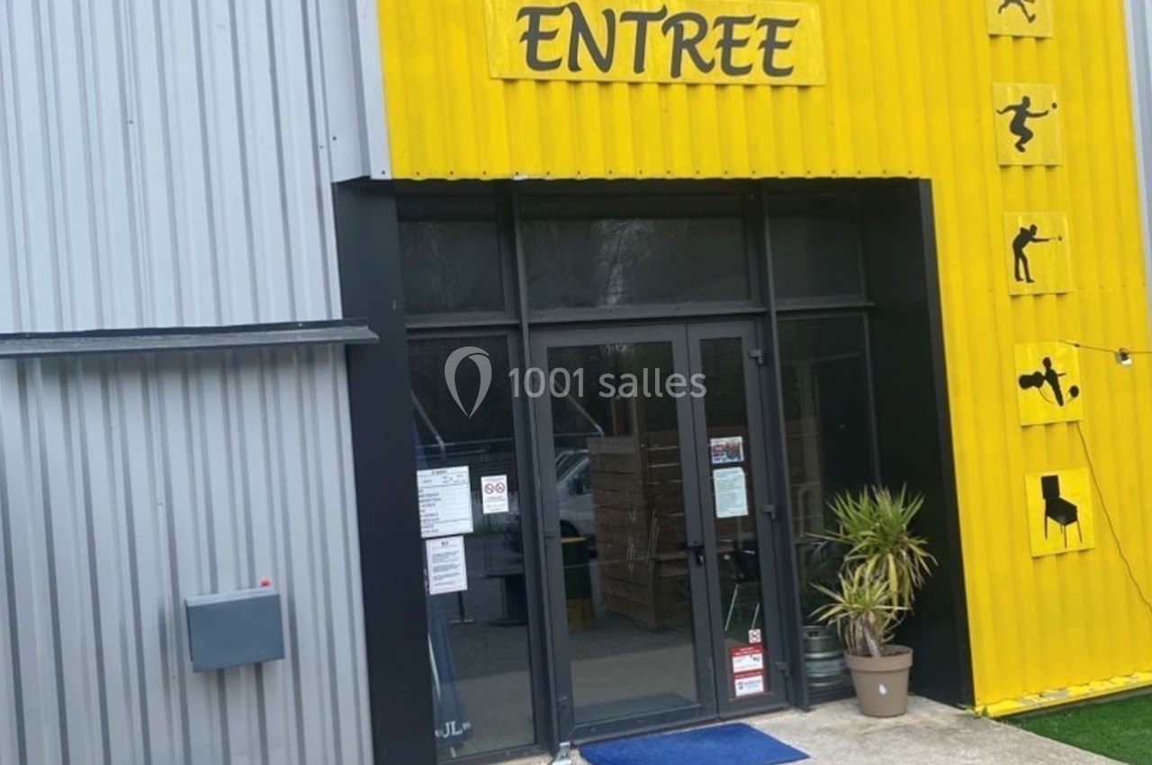 Entrée d'un bâtiment avec une façade jaune et grise, signalée par un panneau ’ENTREE’ et des pictogrammes sportifs.