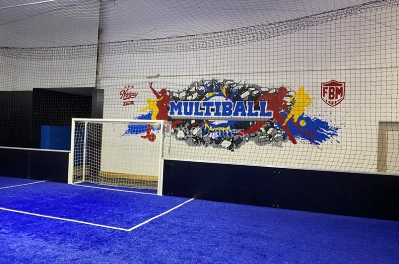 Terrain de sport intérieur avec filet de protection, but de football et mur décoré d'une fresque ’Multiball’.