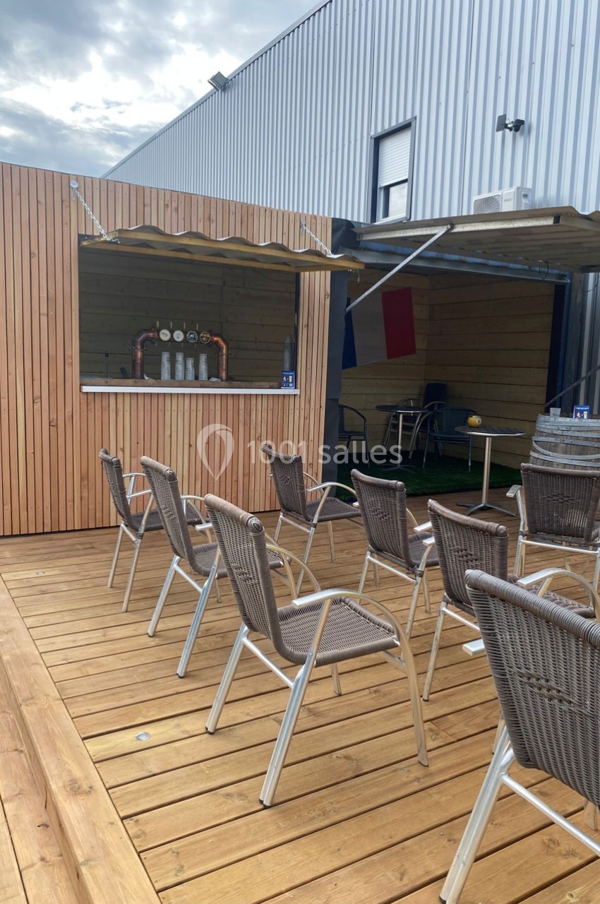 Terrasse en bois avec chaises en osier face à un comptoir extérieur équipé de tireuses à bière.