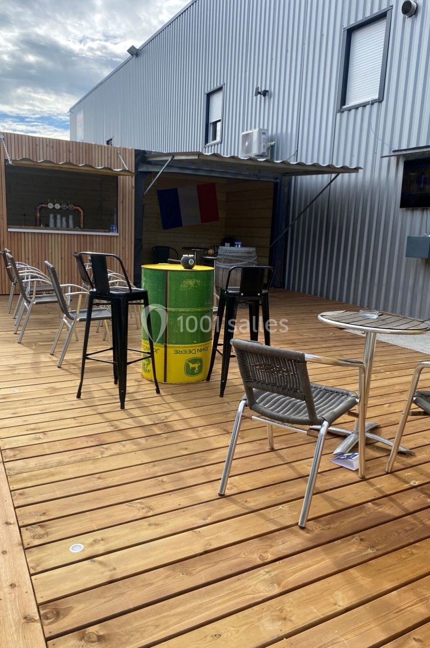 Terrasse en bois avec des tables, des chaises et un bar en fond, décorée de drapeaux français.