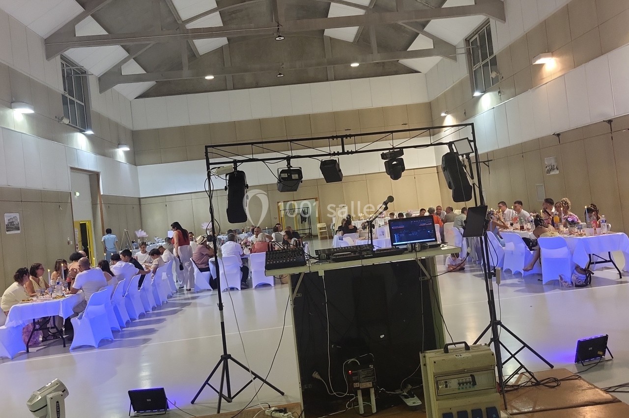 Salle de réception avec des invités assis à des tables décorées, vue depuis une installation de matériel audio.