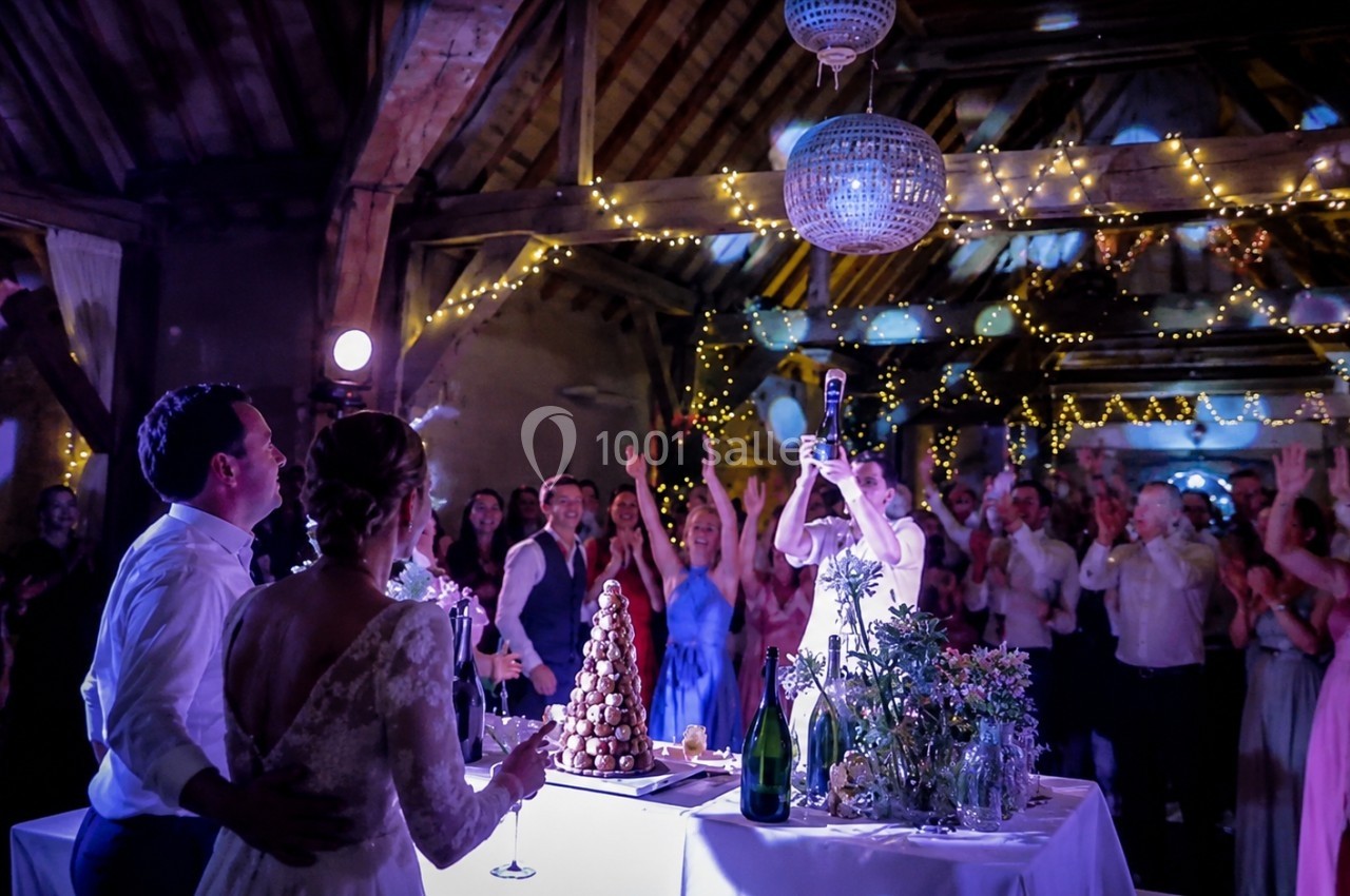 Un couple de mariés regarde leurs invités célébrer dans une salle décorée de guirlandes lumineuses.