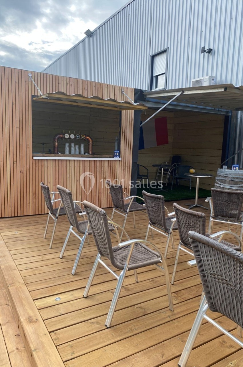 Terrasse en bois avec des chaises en rotin face à un comptoir de bar extérieur sous un auvent.
