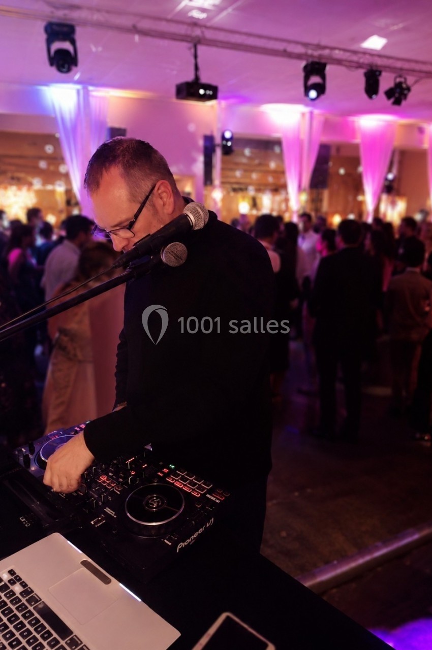 Un DJ mixant de la musique lors d'une soirée festive avec des invités dans une salle éclairée par des lumières colorées.