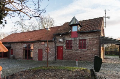 Façade d'une maison orange à trois étages avec toit en tuiles, entourée de bâtiments en briques et d'une cour pavée.
