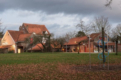 Façade d'une maison orange à trois étages avec toit en tuiles, entourée de bâtiments en briques et d'une cour pavée.