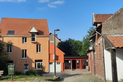 Façade d'une maison orange à trois étages avec toit en tuiles, entourée de bâtiments en briques et d'une cour pavée.
