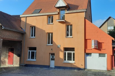 Façade d'une maison orange à trois étages avec toit en tuiles, entourée de bâtiments en briques et d'une cour pavée.