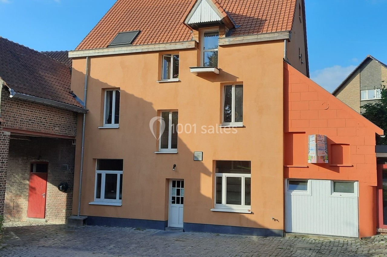 Façade d'une maison orange à trois étages avec toit en tuiles, entourée de bâtiments en briques et d'une cour pavée.
