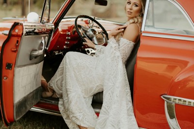 Miniature Germain Photo Reporter #2 Une femme en robe de mariée tient un bouquet de tournesols près d'une voiture ancienne rouge, de nuit.