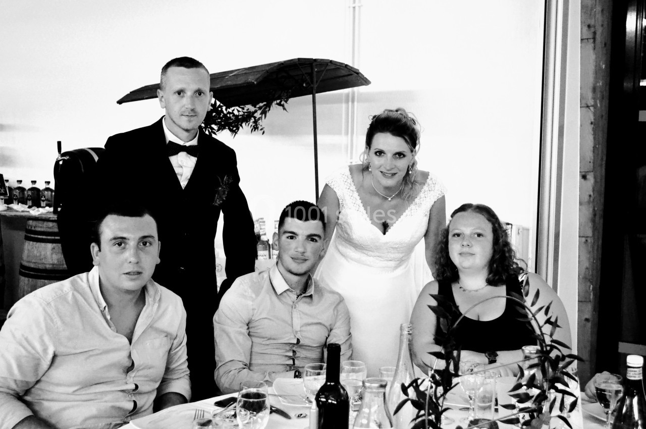 Un groupe de cinq personnes posant autour d'une table lors d'un événement, avec une mariée au centre.